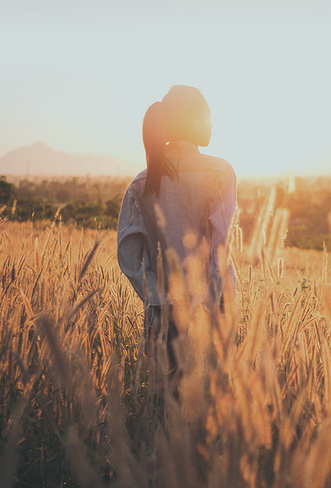 A woman stands in a field and stares into the distance.