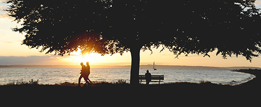 Two people walk along the beach at sunset.